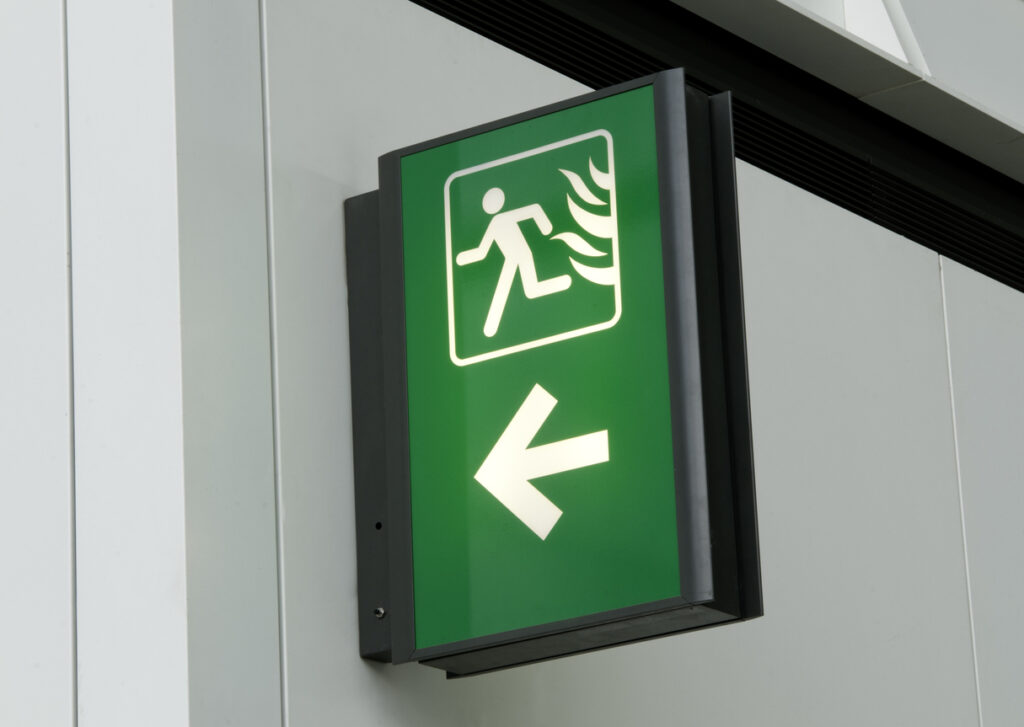 Green and white emergency exit sign on white